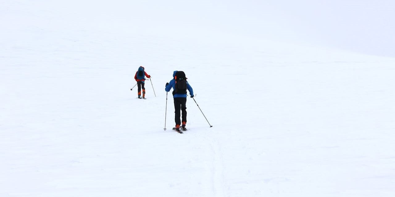 Twee mensen langlaufen door een uitgestrekt besneeuwd landschap, elk met rugzak en skistokken voor balans