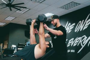 Man traint met dumbbells terwijl een coach hem begeleidt in sportschool