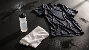 Sportkleding en handdoek nat van zweten tijdens inspanning met bidon voor hydratatie op donkere ondergrond